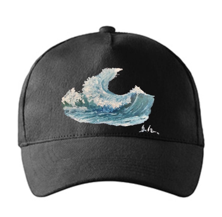 A black baseball cap seen from the front, printed across the crown with a painted breaking wave in blues and white, a small signature beneath it.